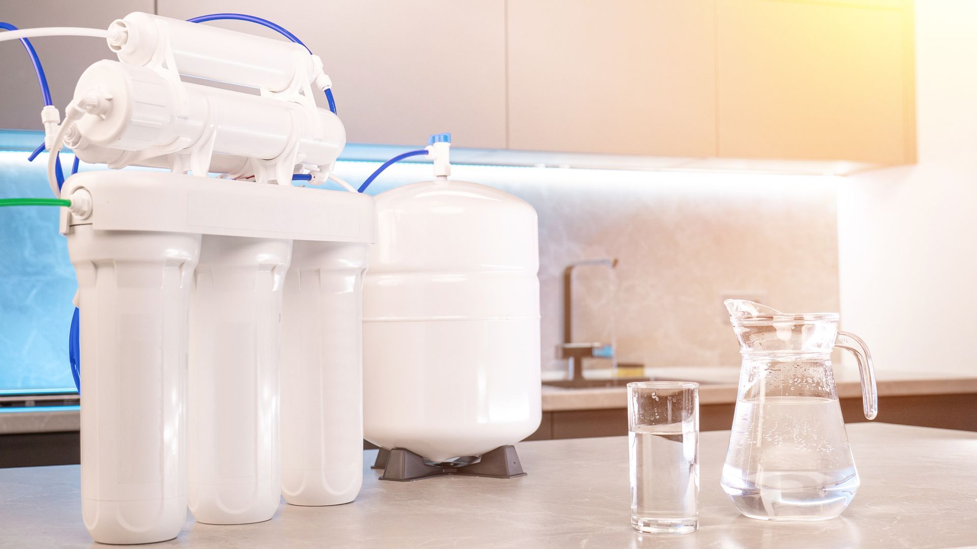 Kitchen countertop with a white water filtration system and clear glass pitcher beside it Kitchen countertop with a white water filtration system and clear glass pitcher beside it