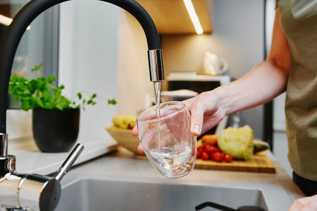 Hand filling a glass with water at a kitchen sink, with fruit and a plant in the background Hand filling a glass with water at a kitchen sink, with fruit and a plant in the background