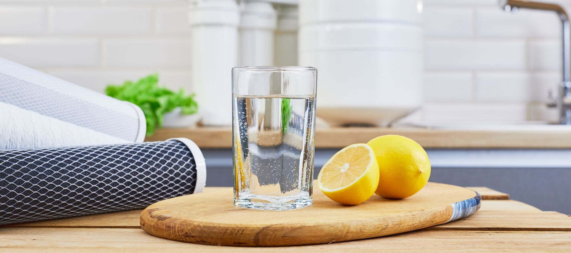 Glass of water with two lemons on a wooden board in a bright kitchen