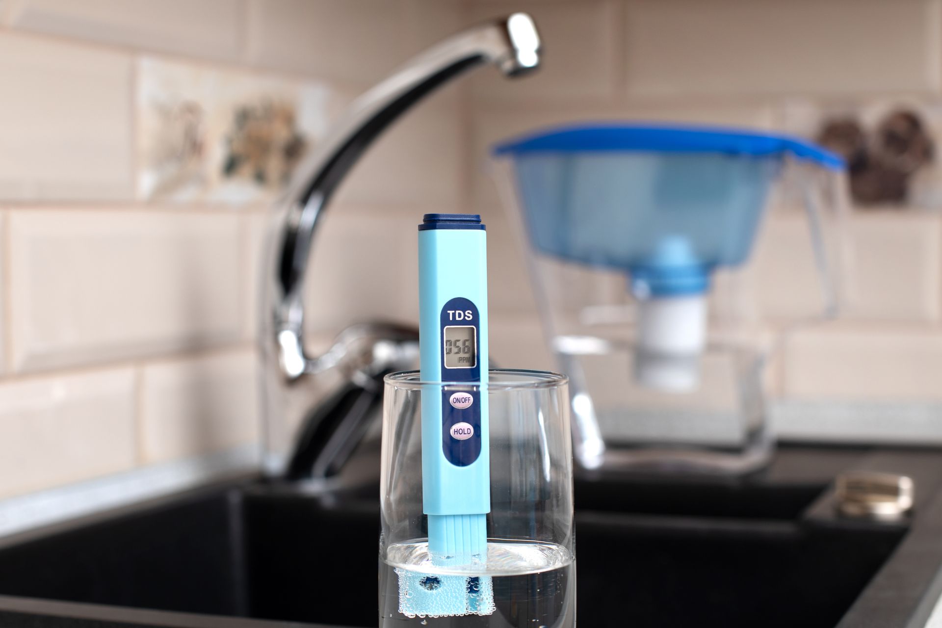 Blue water filter cartridge in a glass at a kitchen sink with a faucet and pitcher in the background Blue water filter cartridge in a glass at a kitchen sink with a faucet and pitcher in the background