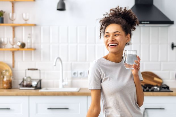 Woman smiling in a bright kitchen, holding a glass of water. Woman smiling in a bright kitchen, holding a glass of water.