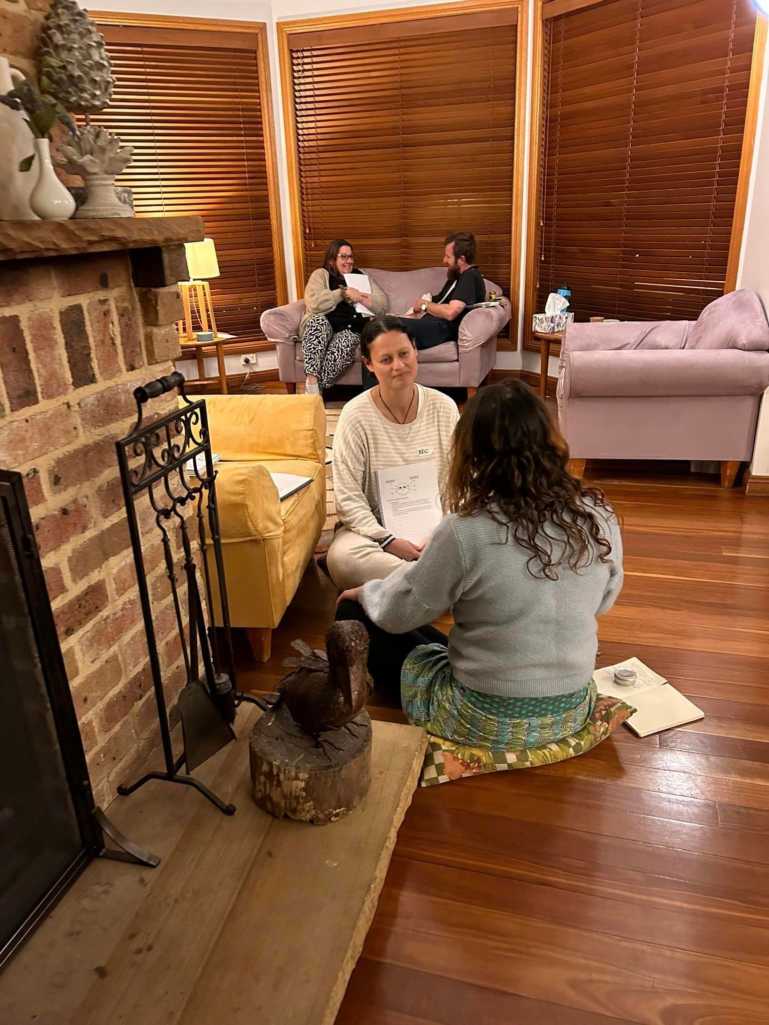 A group of women are sitting on the floor in a living room talking to each other.