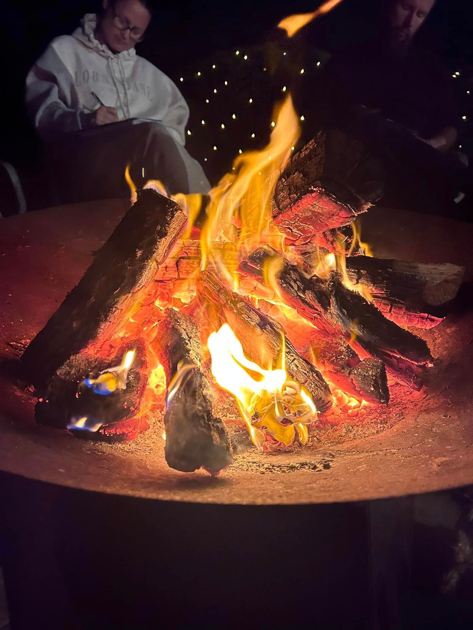 Two people are sitting around a fire pit at night.