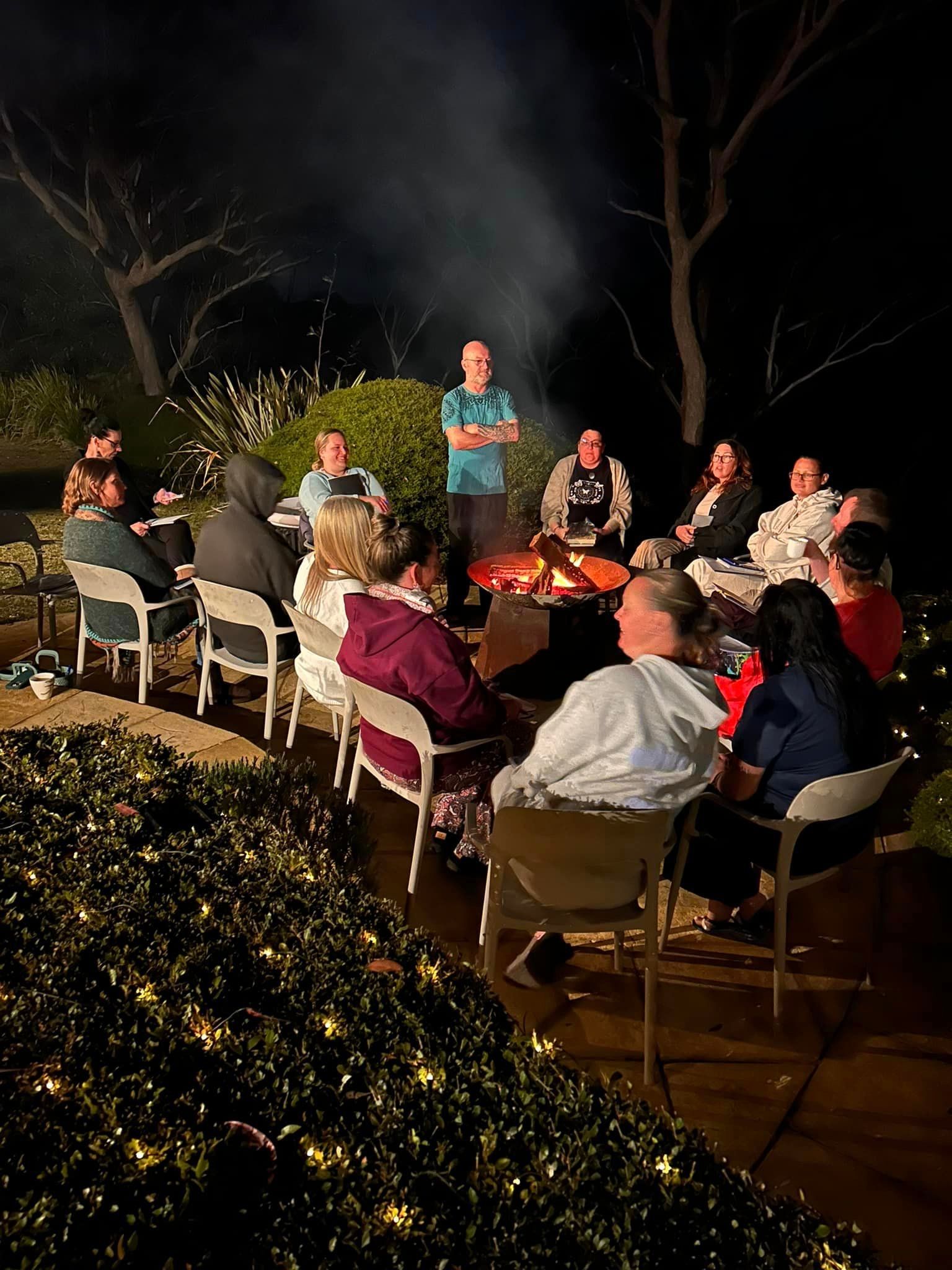 A group of people are sitting around a fire pit at night.