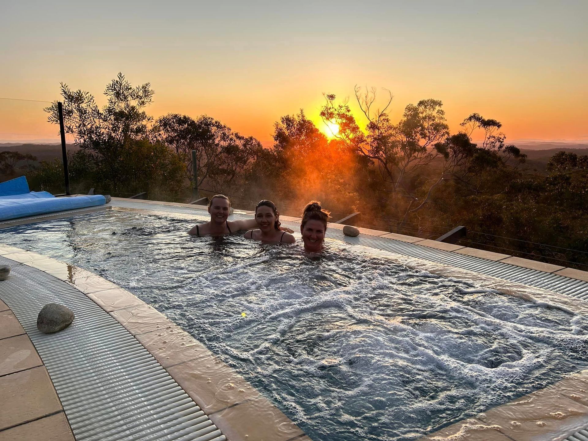A group of people are swimming in a pool at sunset.