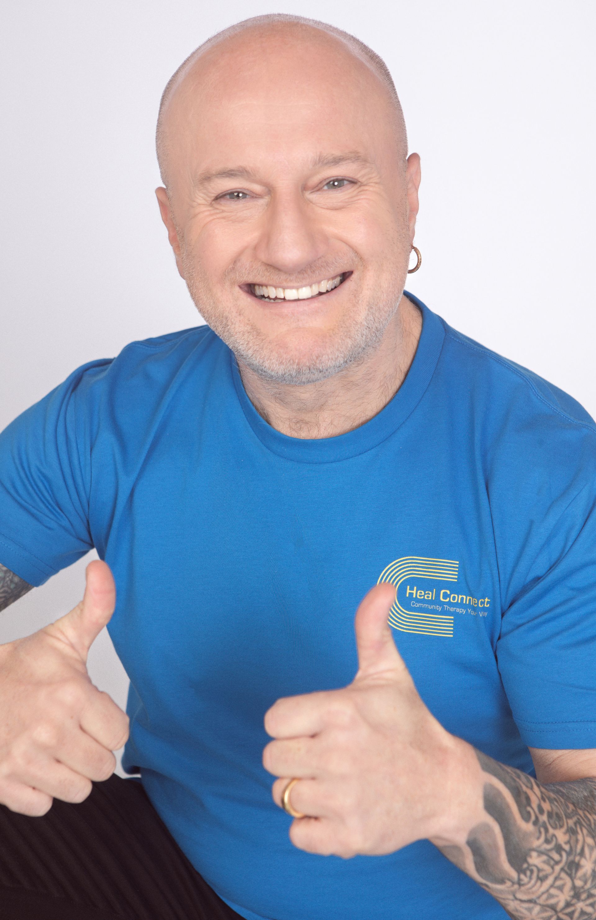 A bald man in a blue shirt is giving a thumbs up