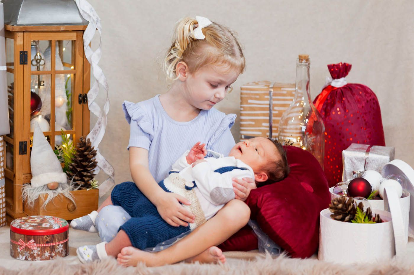 Ein Mädchen hält ein Baby im Arm, beide in einer festlich geschmückten Umgebung. 