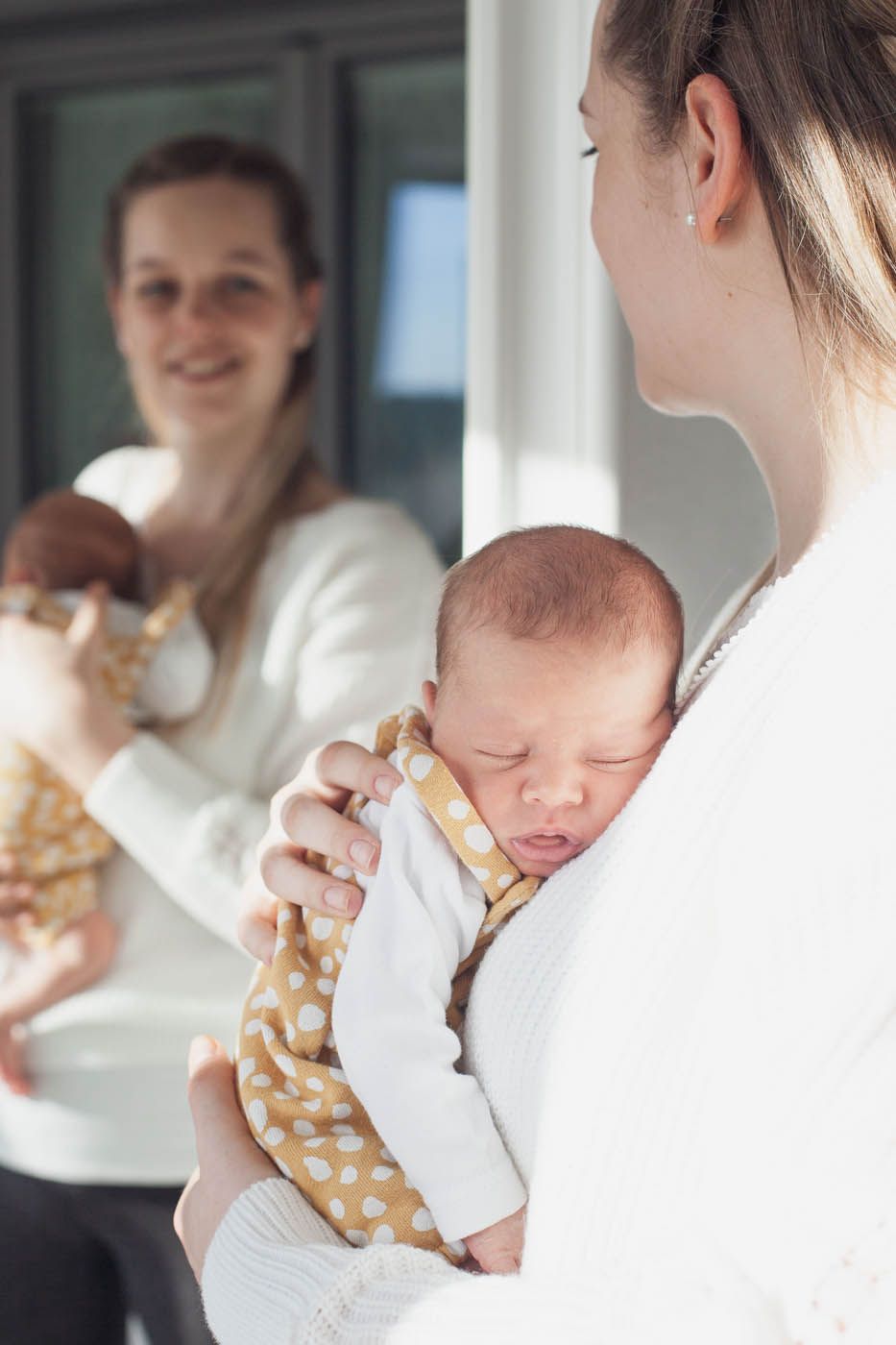Frau hält schlafendes Baby im Arm, Spiegelbild zeigt dieselbe Pose. Beide tragen weiße Pullover.