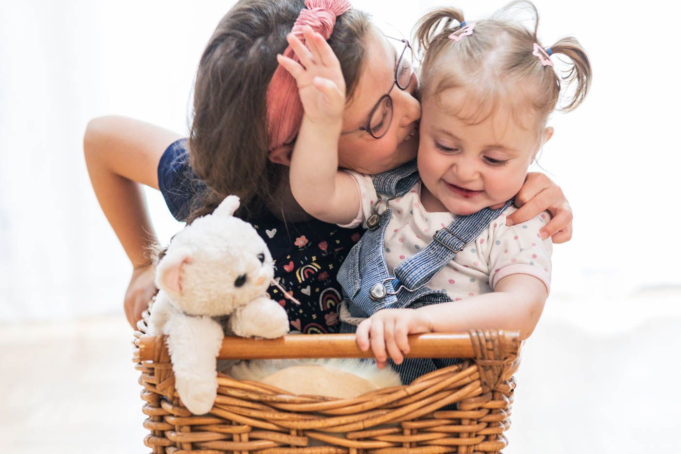 Mädchen umarmt und küsst Kleinkind im Korb mit Teddybär.