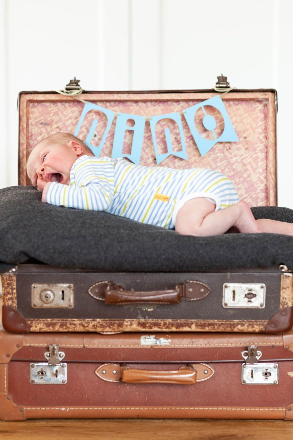 Neugeborenes Baby gähnt auf Koffern mit einem Banner mit der Aufschrift „PAPA“.