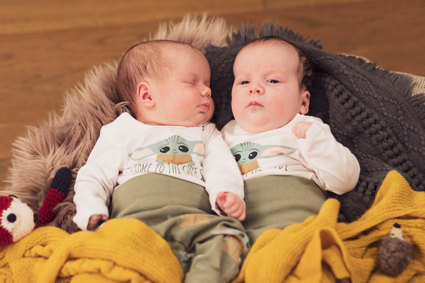 Zwei Babys in passenden Yoda-Shirts liegen in einem gemütlichen Korb mit Decken. Eines schläft, das andere ist wach.