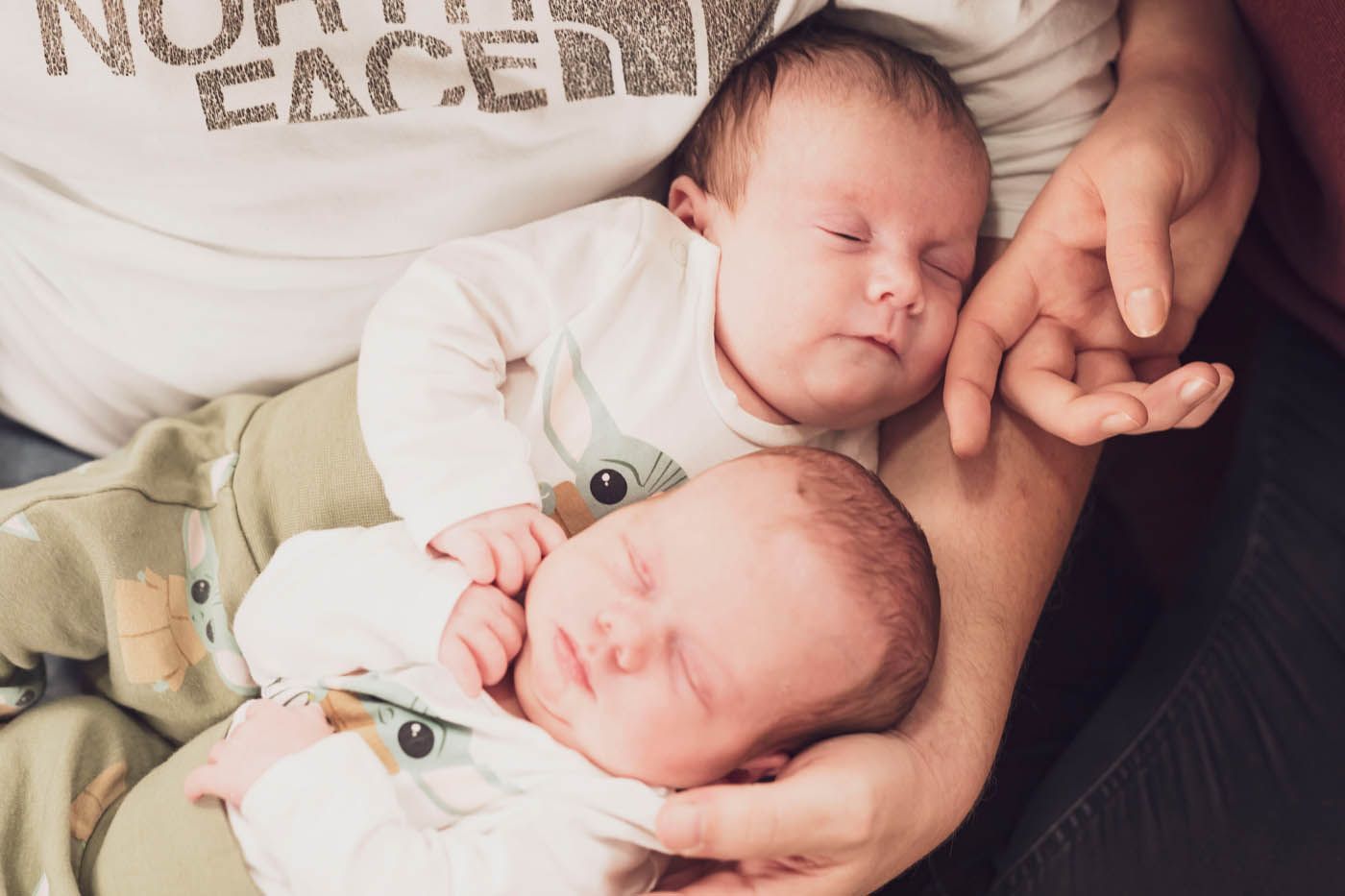 Zwei schlafende Babys, eines über dem anderen, in jemandes Armen.
