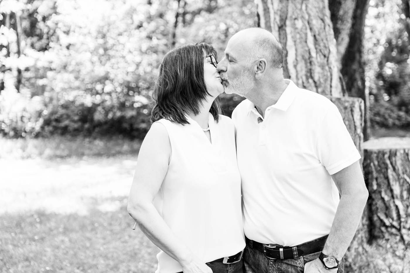 Ein Paar küsst sich im Freien, im Hintergrund Bäume und Laub. Mann und Frau tragen weiße Hemden.