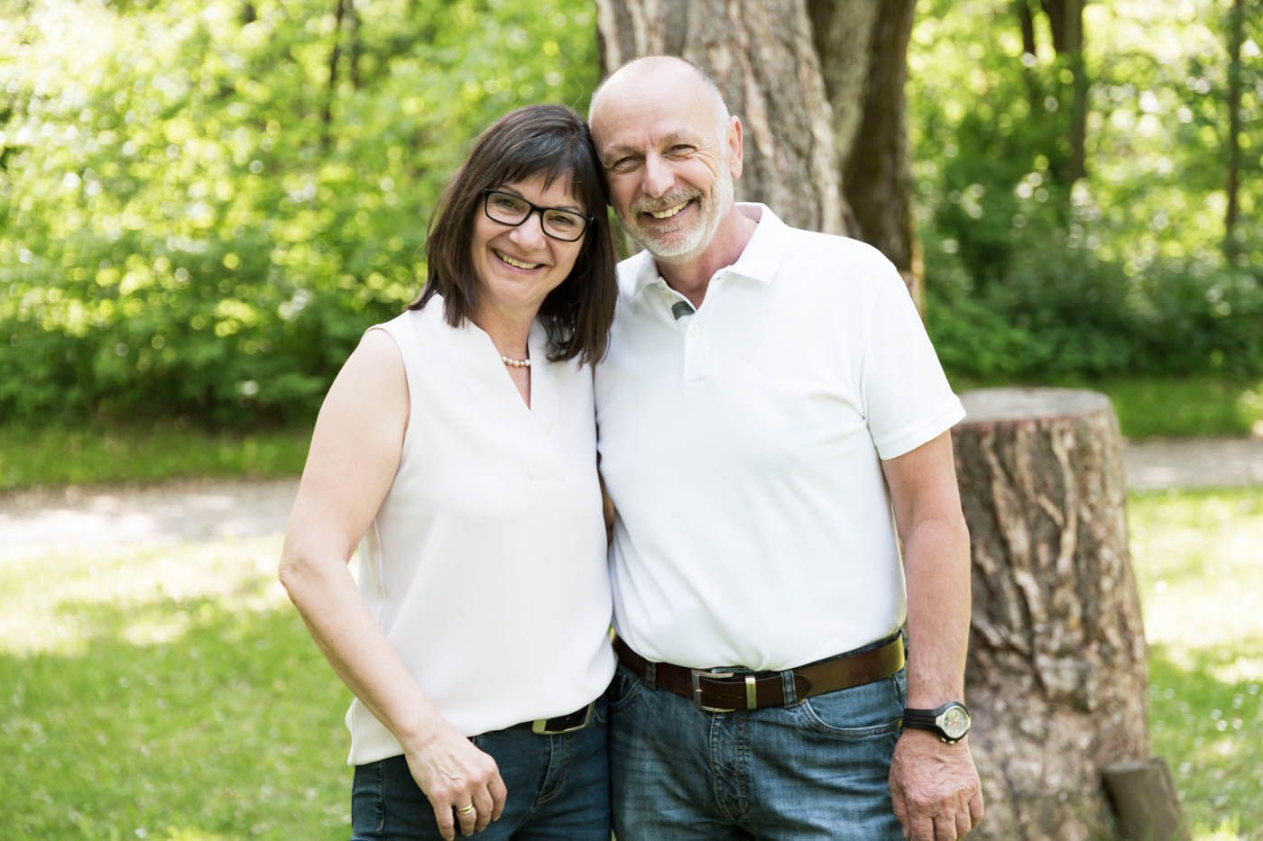 Frau und Mann lächeln und umarmen sich im Freien; beide tragen weiße Hemden und Jeans.