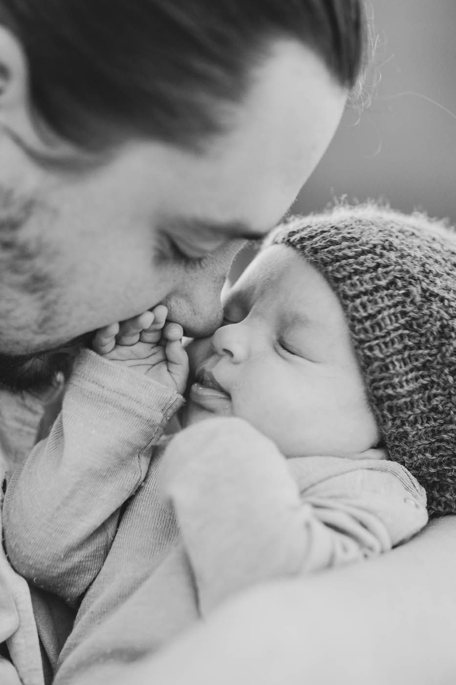 Mann hält und küsst ein schlafendes Baby mit Strickmütze. Schwarz-Weiß-Fotografie.