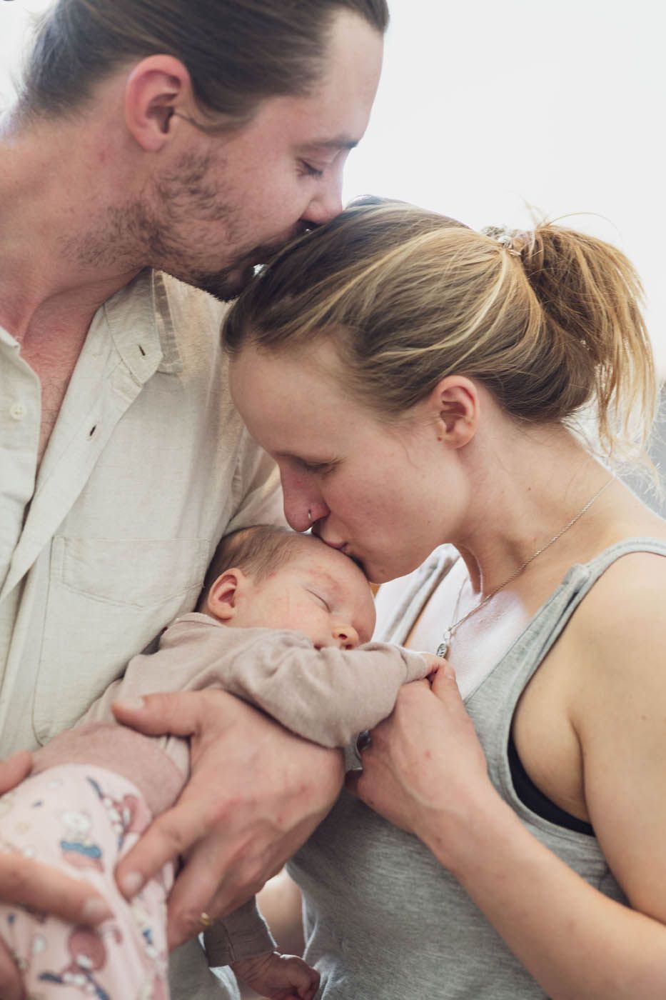 Eltern küssen die Stirn eines schlafenden Babys, das sie im Arm halten.