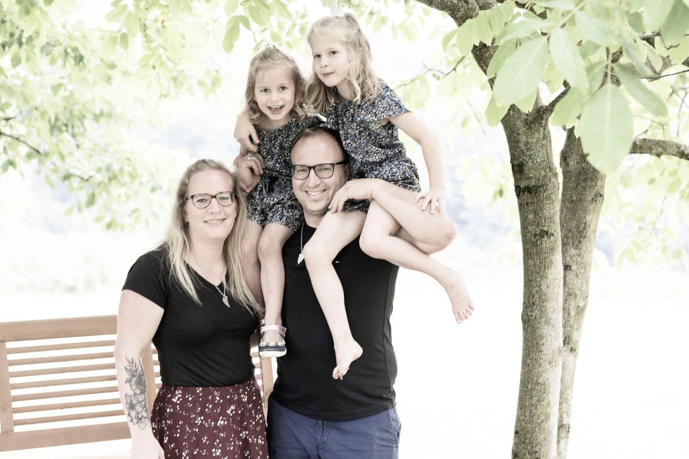 Eine vierköpfige Familie posiert im Freien; zwei kleine Kinder sitzen auf den Schultern ihres Vaters.