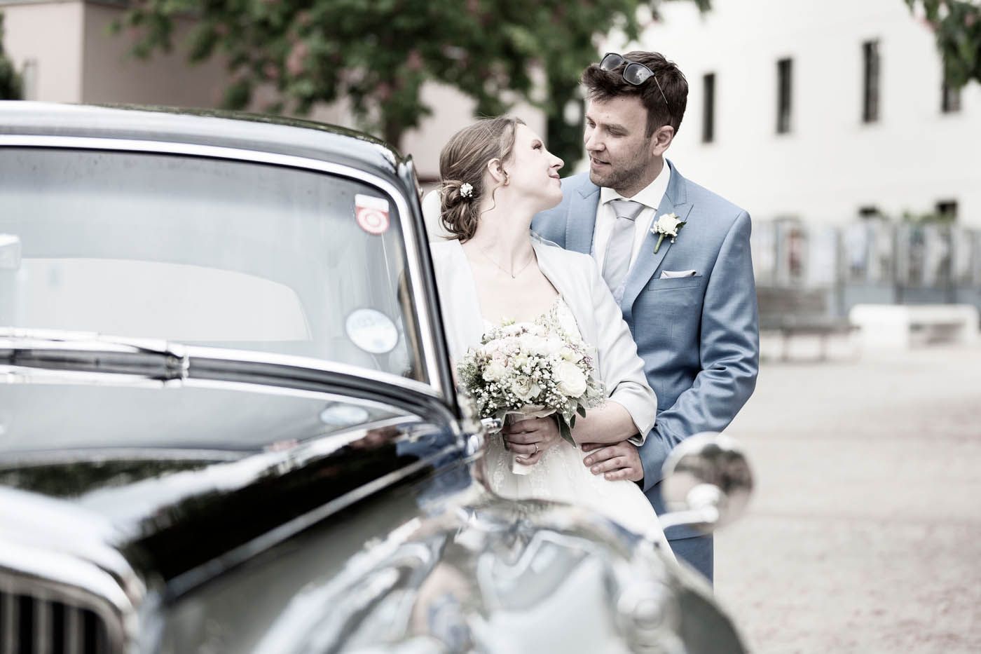 Frischvermählte blicken sich neben einem klassischen schwarzen Auto an;