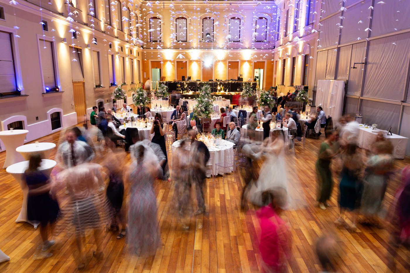 Großer Festsaal, in dem Gäste tanzen und an Tischen unter Lichterketten sitzen.
