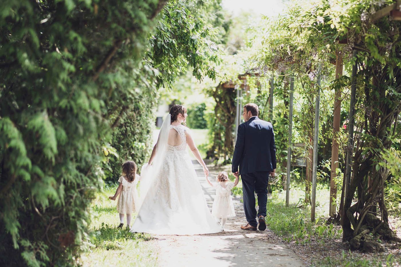 Braut und Bräutigam schreiten Hand in Hand mit zwei kleinen Kindern einen Weg entlang. Hochzeit im Freien.