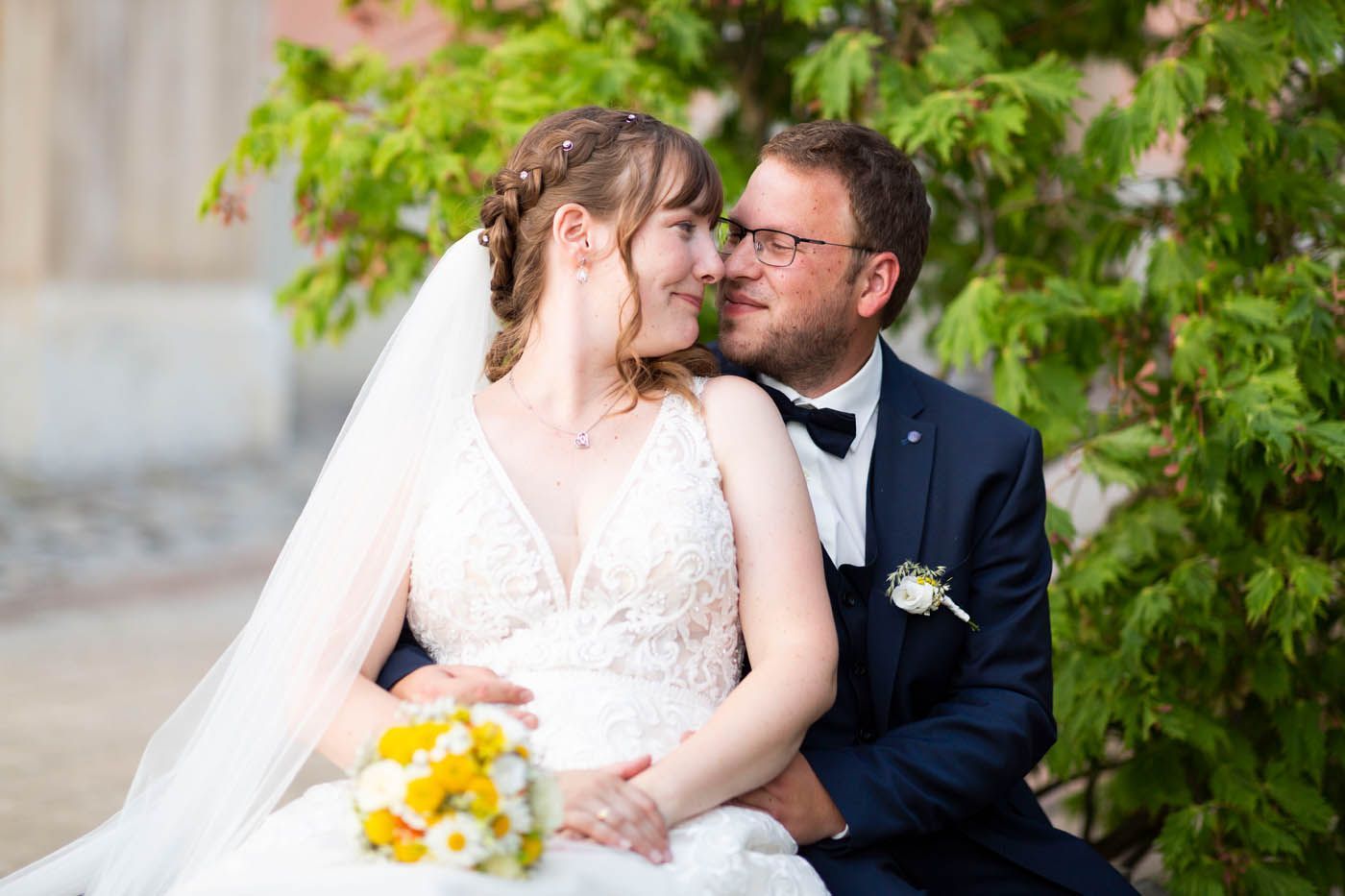 Hochzeitspaar, Braut in weißem Kleid und Schleier, Bräutigam in marineblauem Anzug, umarmen sich, schauen sich an, im Freien.