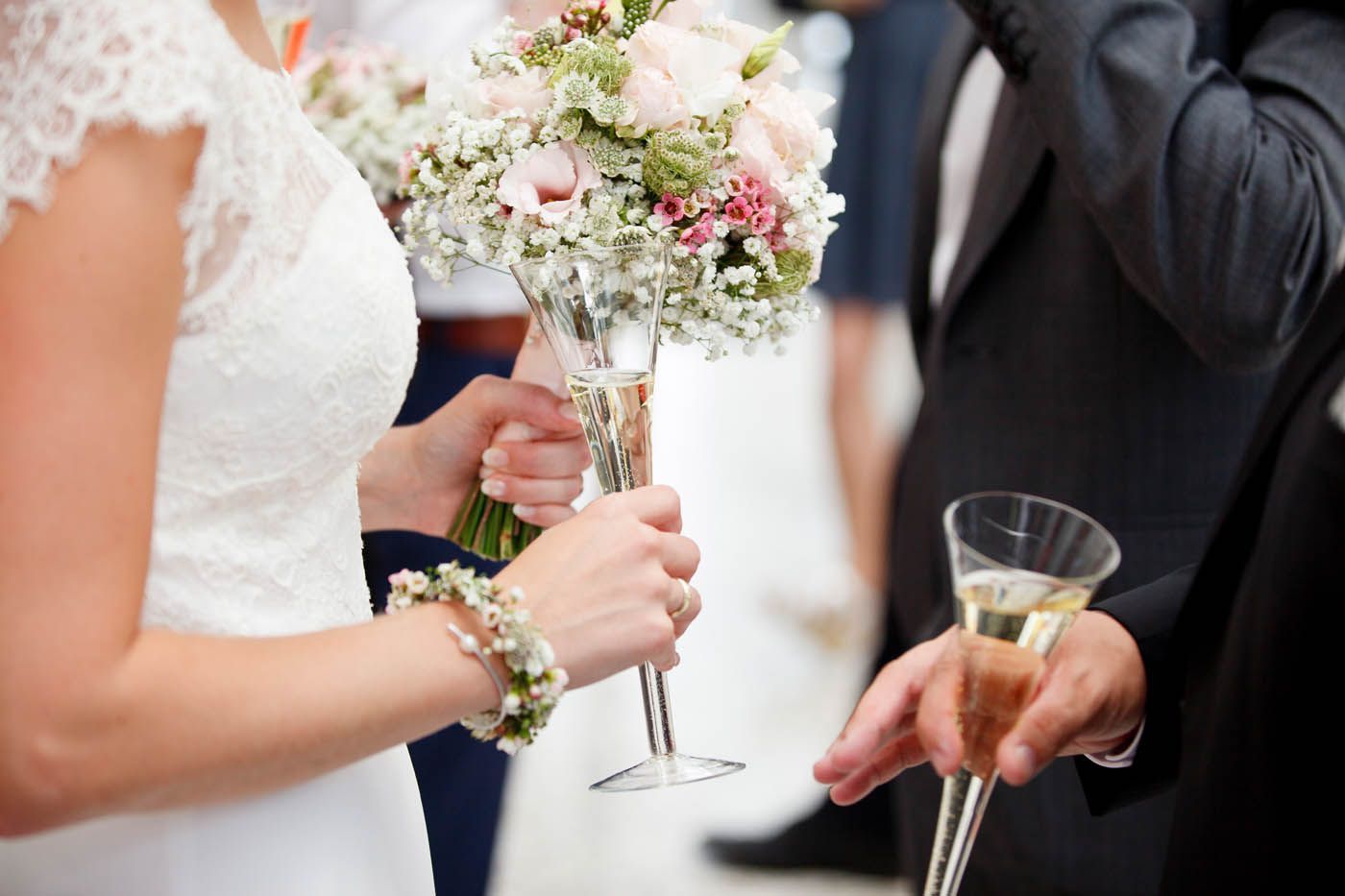 Die Braut hält Blumen und ein Champagnerglas, der Bräutigam bringt einen Champagner-Toast.