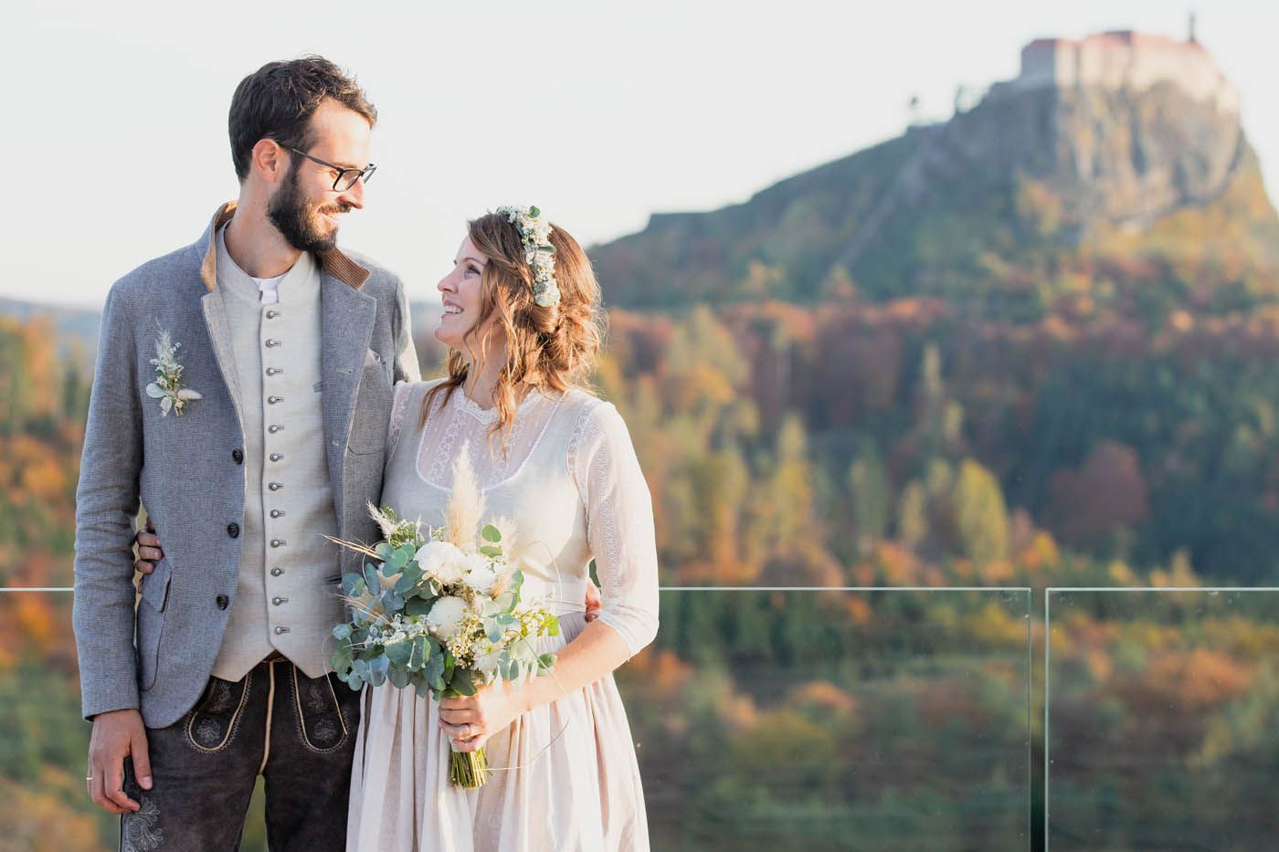 Paar in Hochzeitskleidung vor einer Burg im Hintergrund, Herbstfarben.