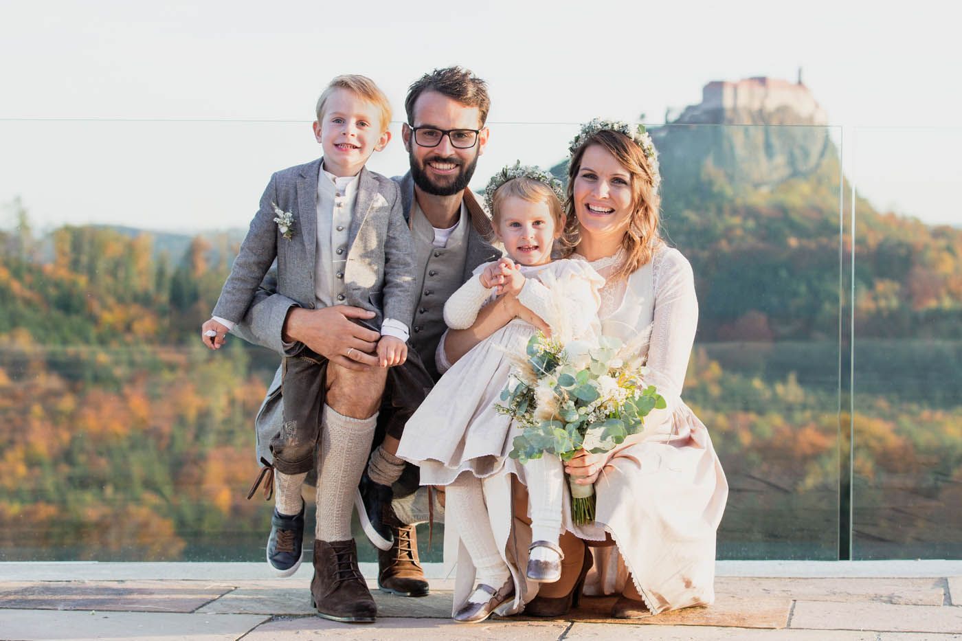 Eine vierköpfige Familie lächelt und posiert im Freien. Im Hintergrund ist eine Burg zu sehen