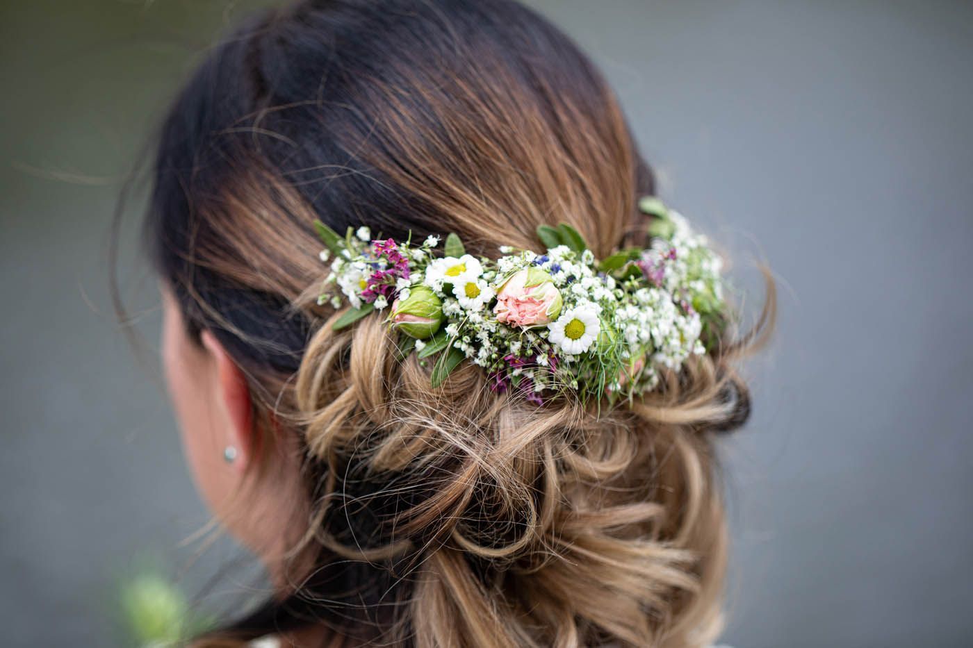 Frau mit hochgestecktem braun-blondem Haar, geschmückt mit einem Blumenkranz.