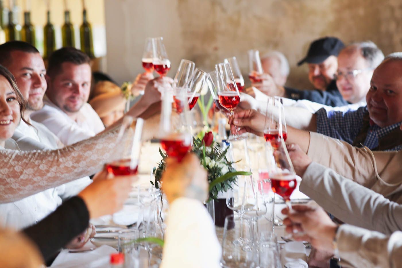 Menschen stoßen an einem Tisch mit Gläsern Rotwein an.