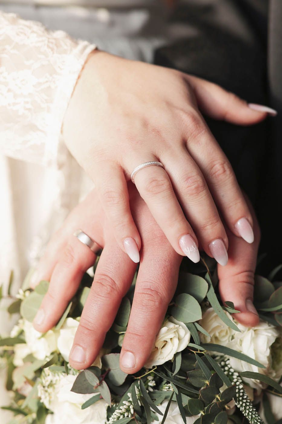 Eheringe an Händen, die über einem Blumenstrauß verschränkt sind.