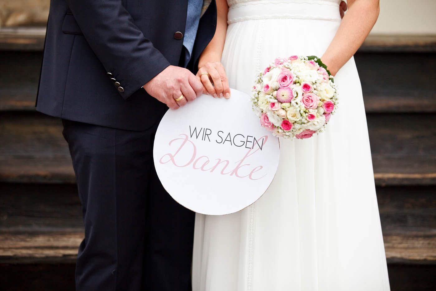 Braut und Bräutigam halten ein Schild mit der Aufschrift „Wir sagen Danke“ und einen Brautstrauß
