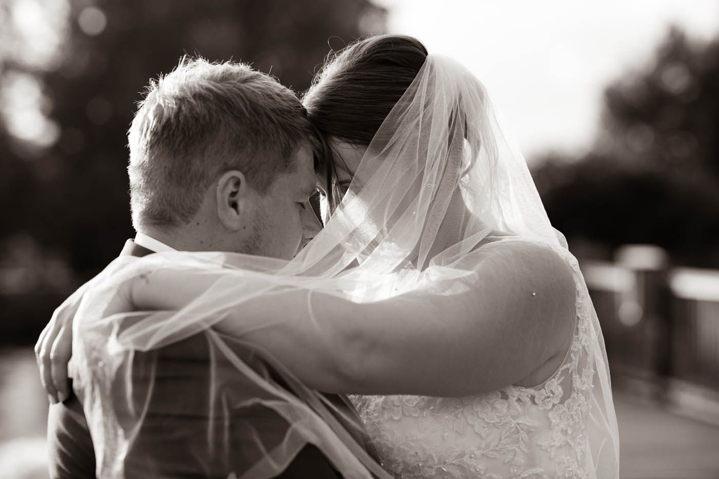 Braut und Bräutigam umarmen sich auf einer Brücke, ihre Köpfe berühren sich;