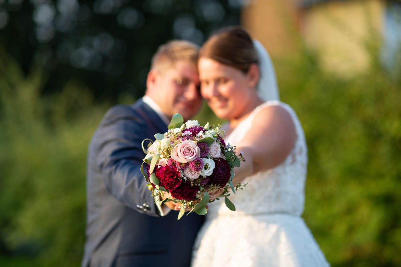 Brautpaar mit einem Blumenstrauß, verschwommener Hintergrund, Szene im Freien.