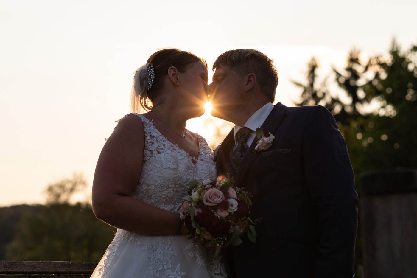 Braut und Bräutigam küssen sich im Gegenlicht der untergehenden Sonne.