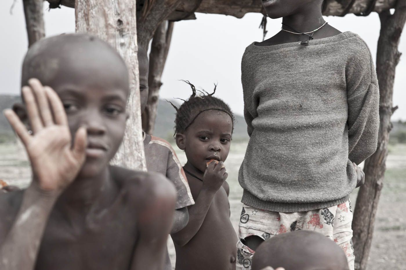 Kinder unter einem provisorischen Unterstand; eines winkt.