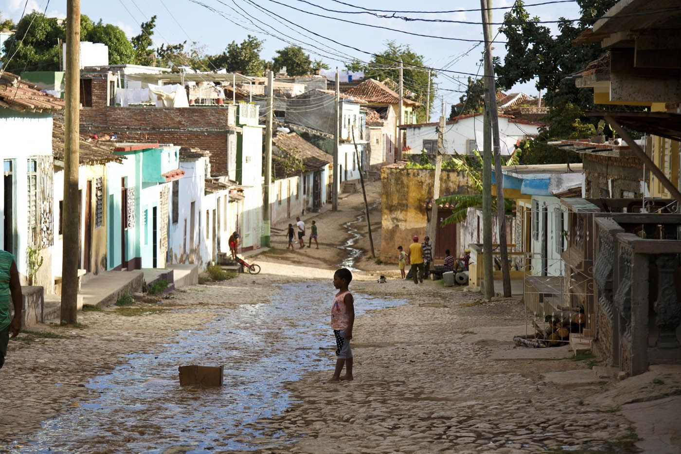 Ein Kind steht in einer verwitterten Straße in einem farbenfrohen Dorf, über deren Straßen Stromleitungen verlaufen.