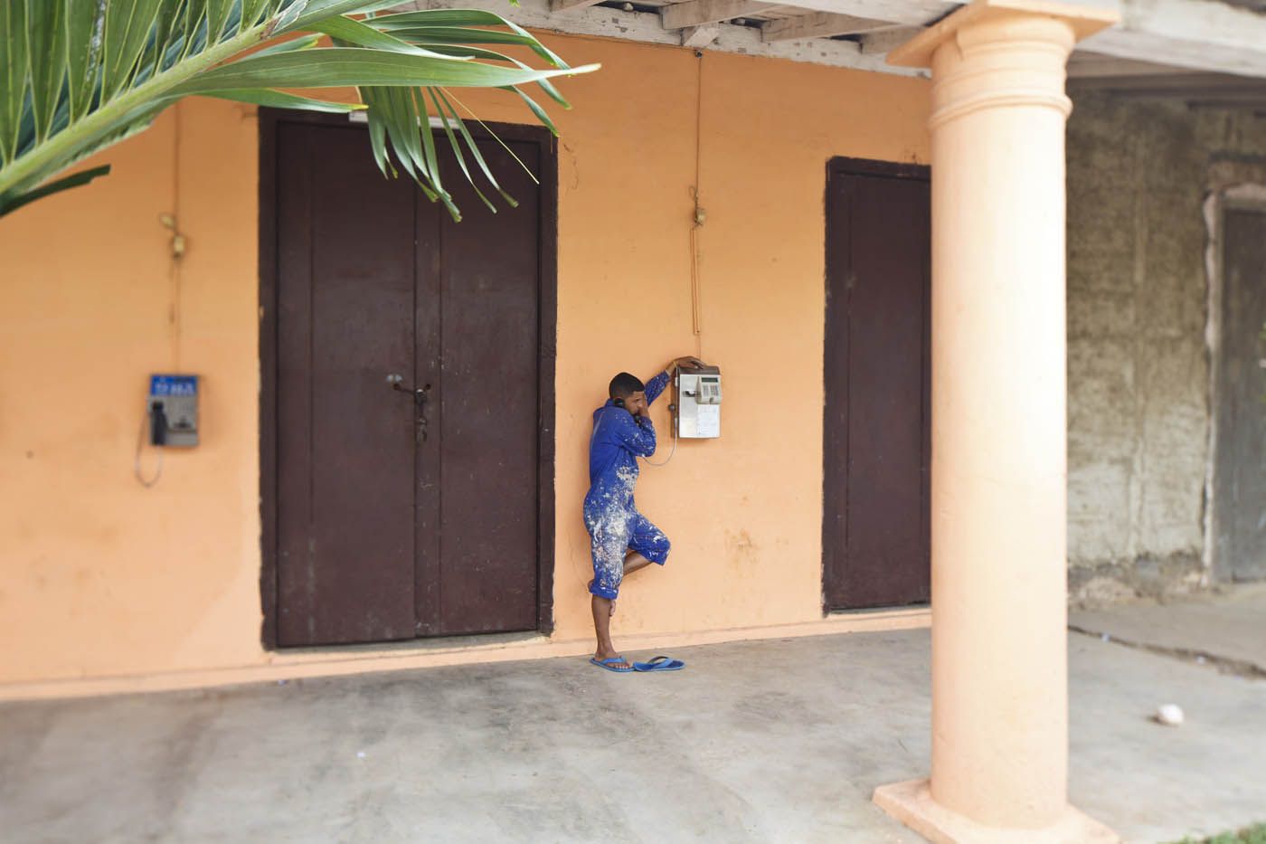 Eine Person steht an einem Gebäude und betrachtet einen Verteilerkasten. Das Gebäude ist orange und braun und weist Säulen und Türen auf.