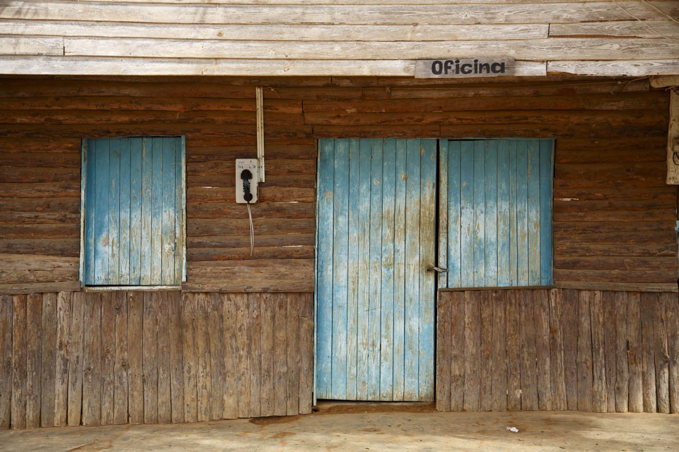 Holzgebäude mit verwitterter blauer Tür und Fensterläden; Schild „Oficina“ über der Tür.