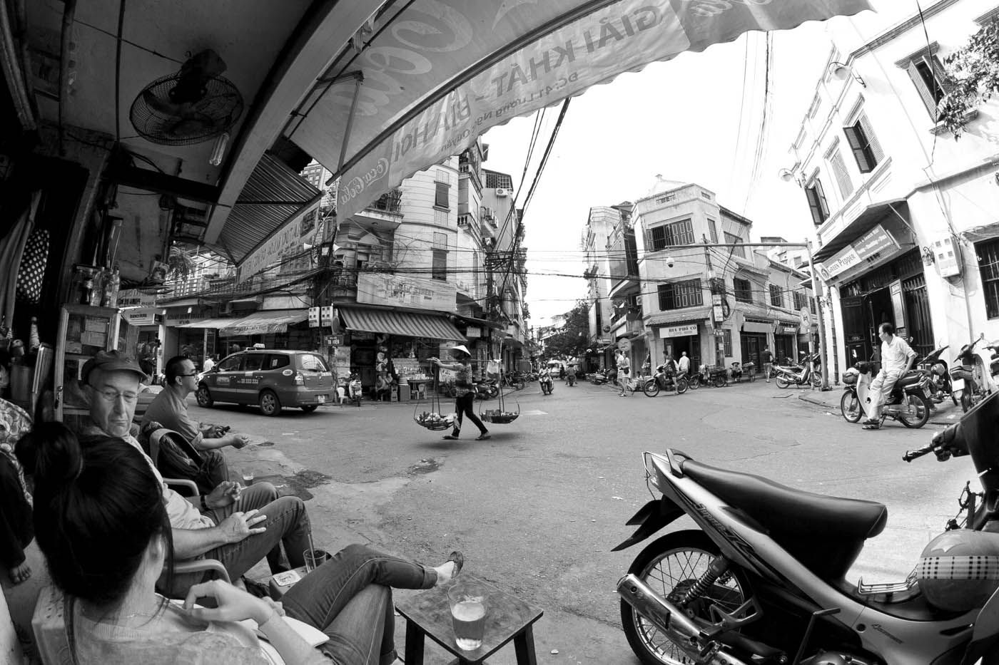 Schwarz-Weiß-Aufnahme einer Straßenszene in Vietnam mit Motorrädern, Gebäuden und Menschen.