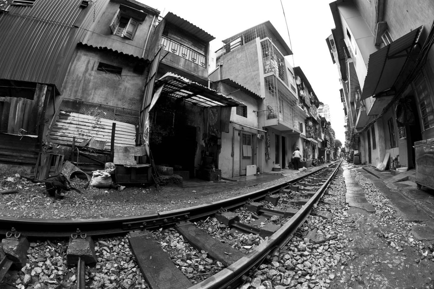 Eisenbahnschienen verlaufen zwischen alten Gebäuden in einer engen, feuchten Gasse.