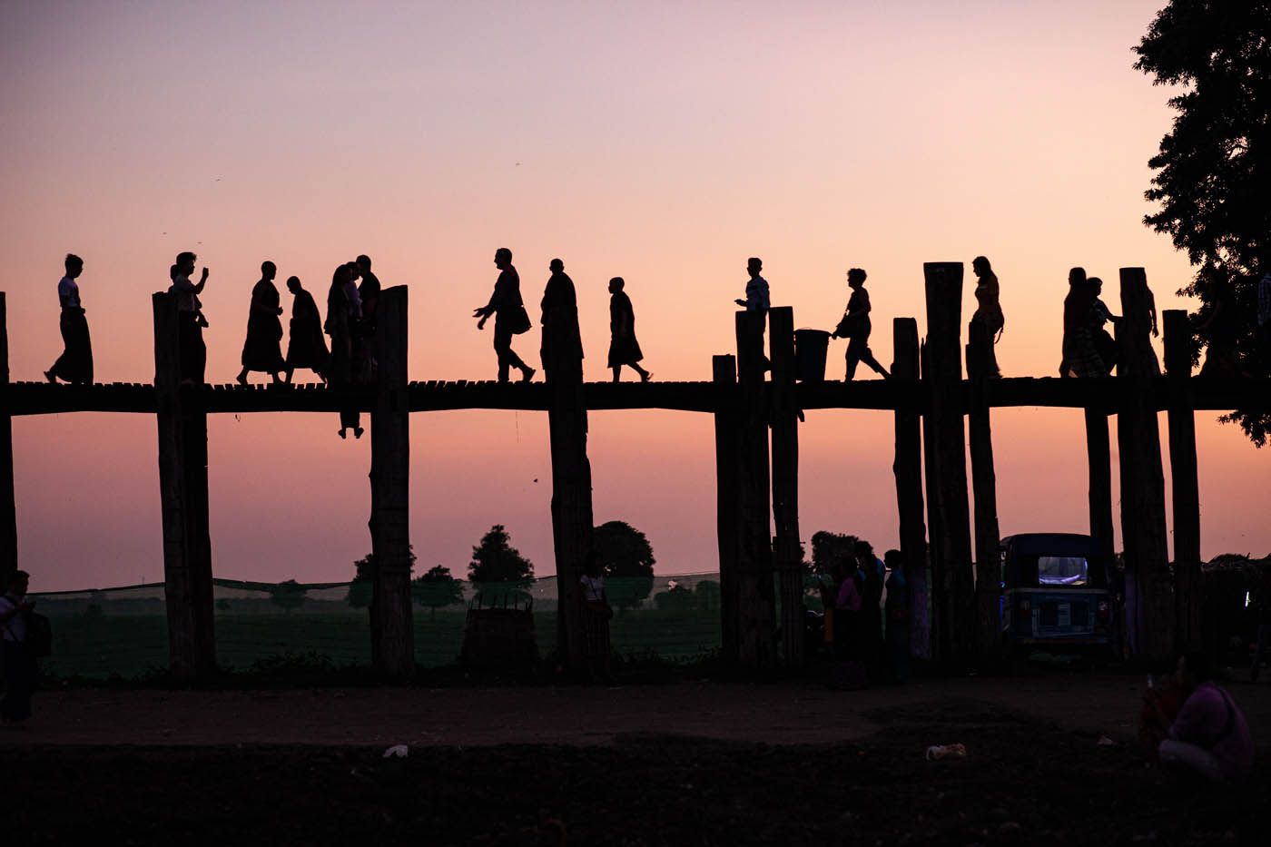 Silhouetten von Menschen, die bei Sonnenuntergang über eine Holzbrücke gehen.