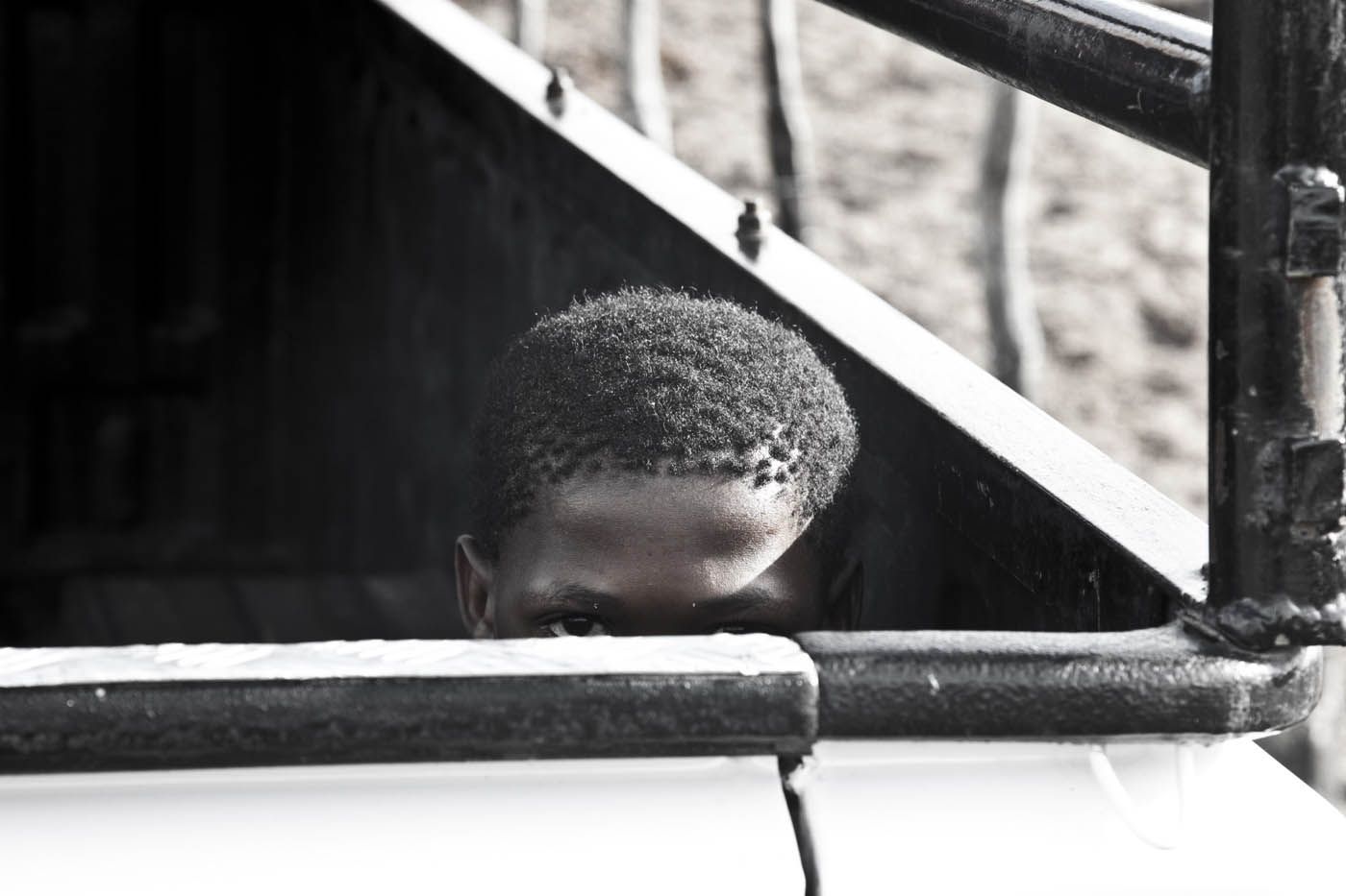 Eine Person späht durch eine dunkle Öffnung, ihre Augen sind sichtbar, umgeben von Metallgittern und Schatten.