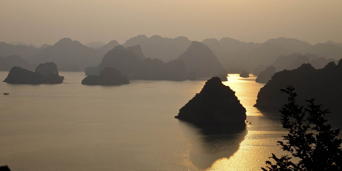 Dunstige Landschaft mit Felsformationen im Wasser, die Sonne spiegelt sich auf der Oberfläche.
