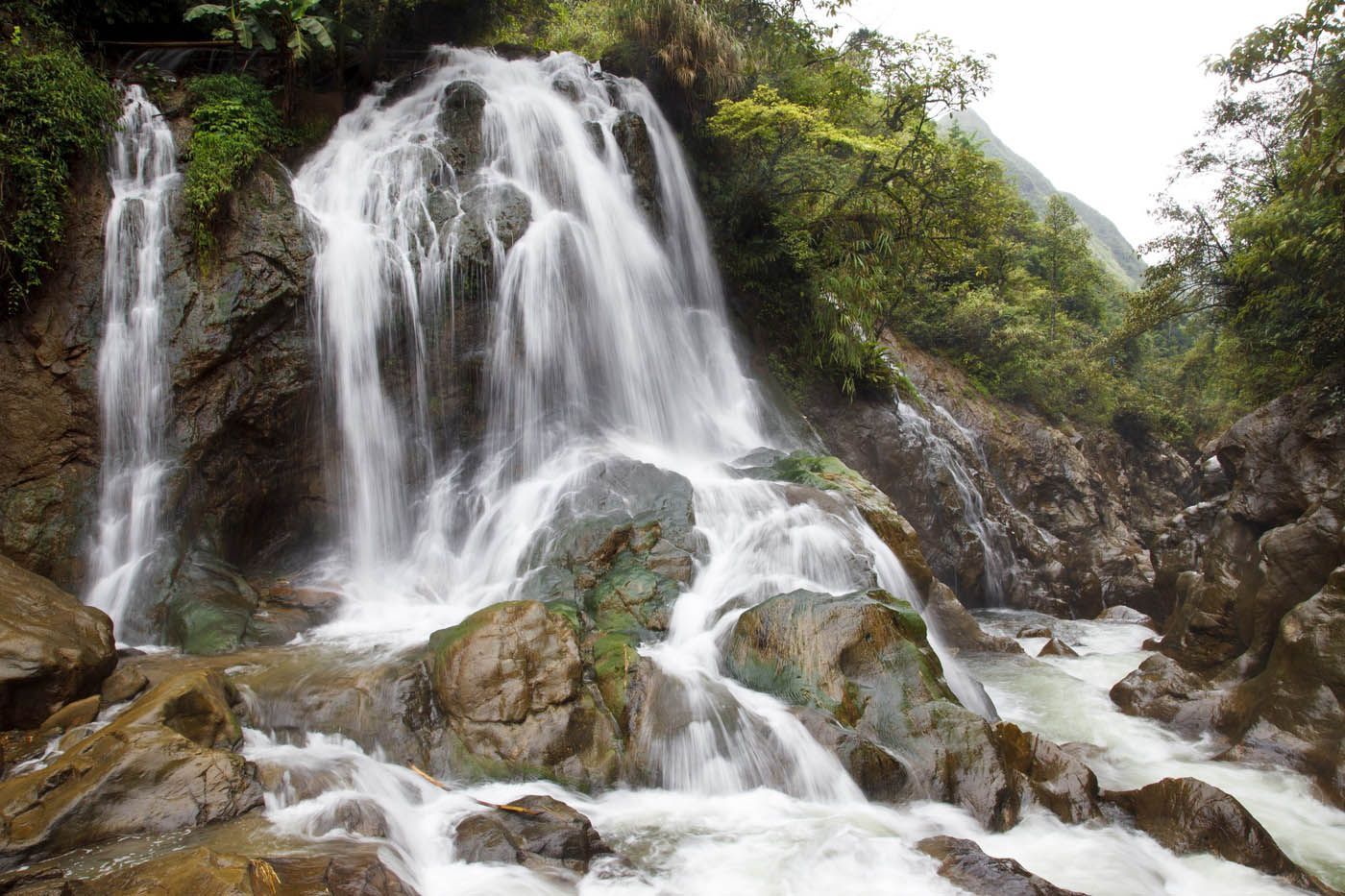 Ein Wasserfall stürzt über Felsen in einer üppig grünen Berglandschaft.