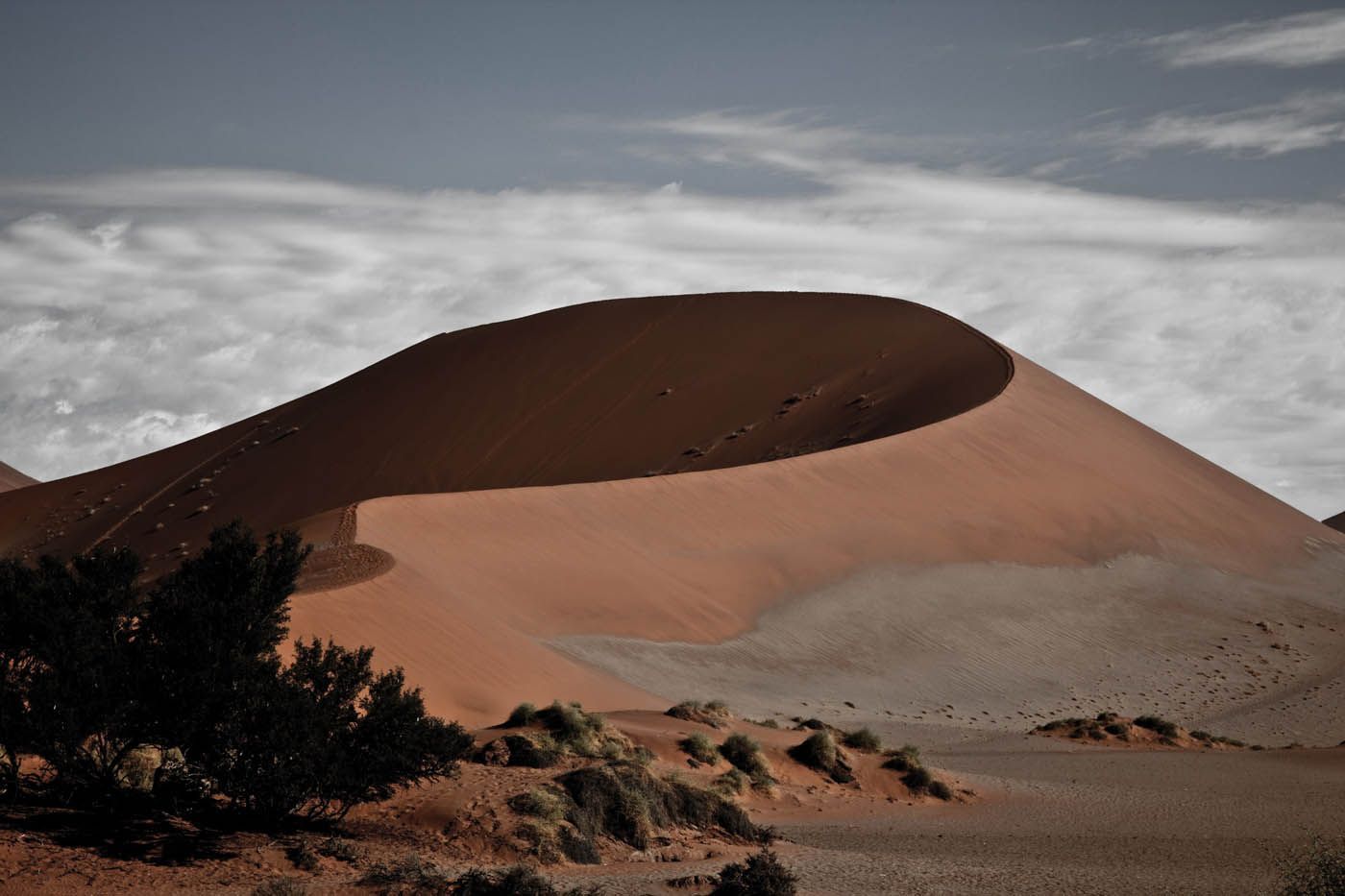 Große orangefarbene Sanddüne unter bewölktem Himmel in einer Wüstenlandschaft.