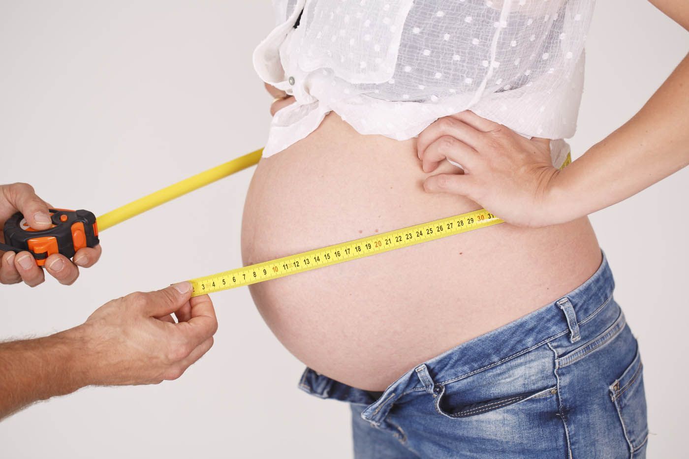 Eine Person misst den Bauchumfang der Schwangeren mit einem gelben Maßband.