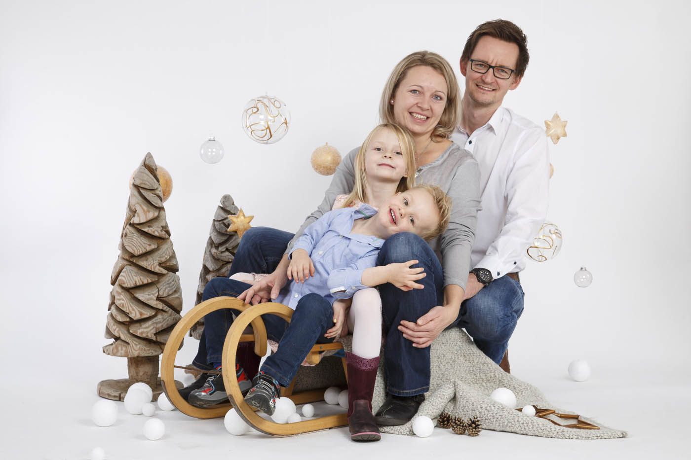 Eine Familie posiert gemeinsam vor Weihnachtsdekorationen; zwei kleine Kinder, Mutter und Vater lächeln.