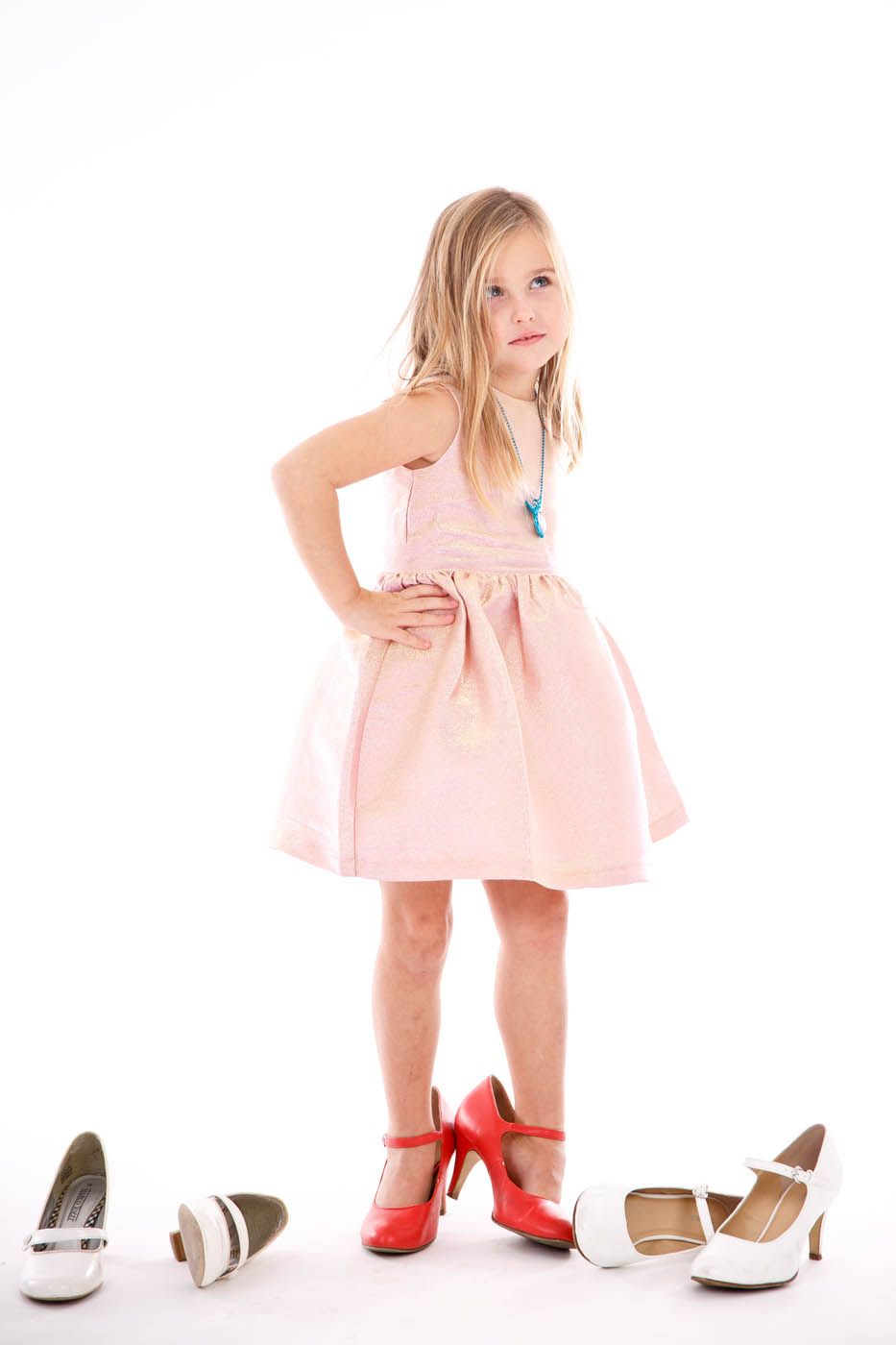 Mädchen in einem rosa Kleid, das mit roten High Heels an den Füßen steht