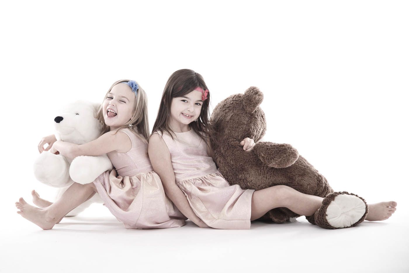 Zwei Mädchen in rosa Kleidern sitzen Rücken an Rücken mit Teddybären